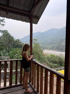 eine Frau, die auf einer Veranda steht und auf die Berge blickt in der Unterkunft Sunset Riverside Cottage, Umngot River in Dawki