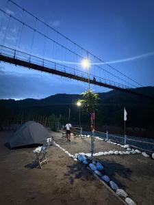 eine Brücke mit einem Zelt und einer Person, die mit einem Hund spazieren geht in der Unterkunft Sunset Riverside Cottage, Umngot River in Dawki + 3 Fotos