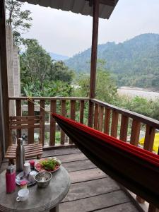 eine Hängematte auf einem Holzdeck mit einem Tisch und Essen in der Unterkunft Sunset Riverside Cottage, Umngot River in Dawki