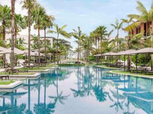 Una piscina en un resort con palmeras y sombrillas. en Pullman Khao Lak Resort, en Khao Lak
