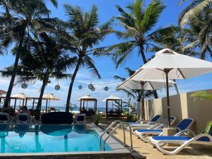 una piscina con sillas y sombrillas y palmeras en Nico Beach Hotel, en Hikkaduwa