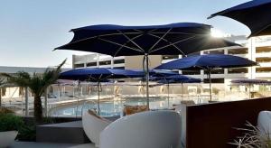 a pool with blue umbrellas and white chairs and tables at Luxury Suites International by Vdara in Las Vegas