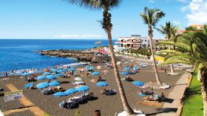 a beach with palm trees and people laying on the sand at Be five Playa La Arena in Puerto de Santiago