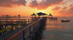 a pier with a boat on the water at sunset at Grand Darmo Suite by AMITHYA in Surabaya