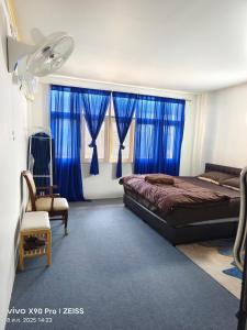 a bedroom with blue curtains and a bed and a fan at Banphe​ Hostel in Ban Phe