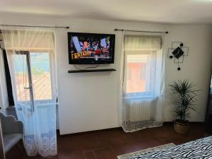 a living room with a tv on the wall and two windows at Dina’s Flower House in Lierna