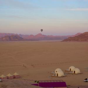 a hot air balloon flying over a desert with tents at Rum Jordan camp and tours in Wadi Rum