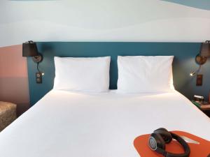 a white bed with two pillows and a hat on it at Ibis Styles Miramas in Miramas