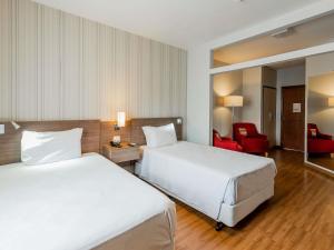 a hotel room with two beds and a red chair at Ibis Styles Campinas Alphaville in Campinas