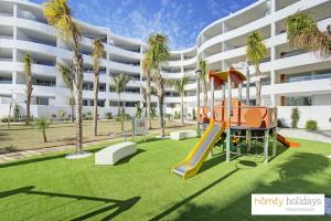 un parque infantil frente a un edificio con palmeras en Homity Holidays - Playa Granada - Mar de Fabiola, en Motril