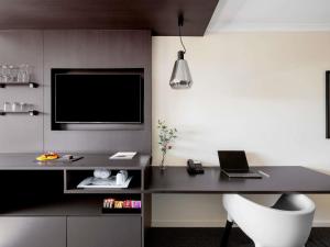 a room with a desk with a laptop and a tv at Mantra on Northbourne in Canberra