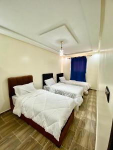 a room with three beds with white sheets and a blue curtain at Residence Hamada Laayoune - Family & Traveler Apartments in Oulad Akkou
