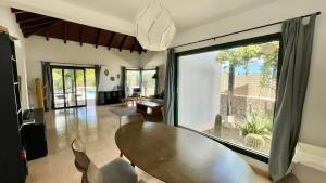 Un comedor con una mesa y un gran ventanal. en Villa spacieuse et lumineuse avec piscine Chauffée, en La Oliva