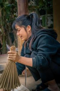 a woman is sitting on the ground working on a broom at Nùng An homestay in Quảng Uyên