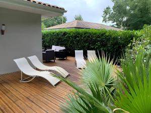 a wooden deck with white chairs and plants at Villa jacuzzi entre Lac et Ocean in Cazaux