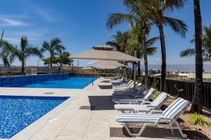 - une rangée de chaises longues et un parasol à côté de la piscine dans l'établissement Oasis Villa Salalah, à Raysūt