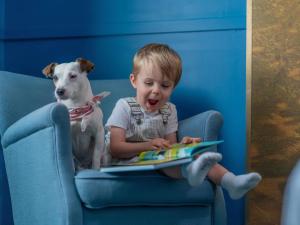 a young boy sitting in a chair with a dog at Hotel Novotel Domaine de Maffliers - Paris Val-d'Oise in Maffliers