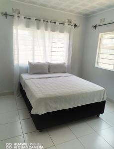 a bed in a white bedroom with a window at Wamz Apartments And Tours B in Livingstone
