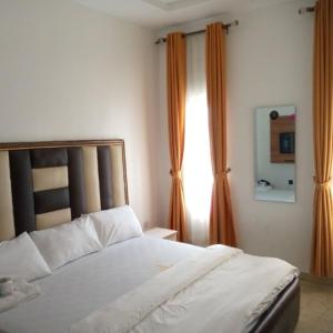 a bedroom with a white bed and orange curtains at The Cartwright Suite and Lounge in Warri