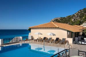 a pool with chairs and umbrellas next to the ocean at Sunset Premium Studio A in Agios Nikitas