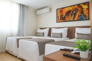 two beds in a hotel room with a tv on the wall at Vida Plaza Hotel in Brasília