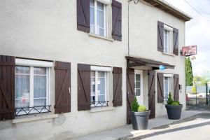 FromentièresにあるGîte Comme Chez Soi En Champagneの茶色のシャッター付き窓と鉢植えの植物がある白い建物