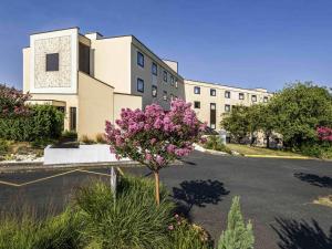a building with purple flowers in a parking lot at Mercure Tours Sud in Joué-lès-Tours