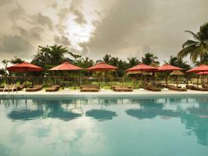a swimming pool with red umbrellas and chairs and tables at Novotel Cotonou Orisha in Cotonou