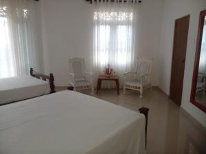 a bedroom with two beds and two chairs and windows at Ananthaya- the infinity in Wadduwa