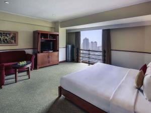 ein Hotelzimmer mit einem großen Bett und einem Fernseher in der Unterkunft Mercure Jakarta Kota in Jakarta