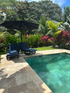 an umbrella and two chairs next to a swimming pool at Tropical Oasis in Ojochal in Ojochal