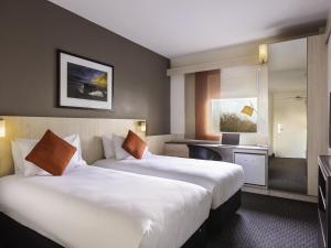 a hotel room with two beds and a desk at ibis Auckland Ellerslie in Auckland +27 photos