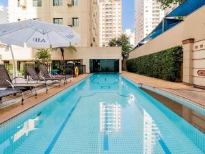 a swimming pool with an umbrella and some buildings at Mercure São Paulo Ibirapuera Privilege in Sao Paulo