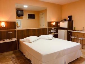 a bedroom with a large white bed and a kitchen at Exos Castelinho Motel in Concordia