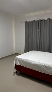 a bed in a white room with a curtain at Quarto Porto in Porto Seguro
