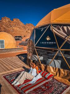 Una mujer tumbada sobre una alfombra bajo una sombrilla en Laver wadi rum, en Wadi Rum