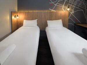 two beds in a room with white sheets at ibis Curitiba Batel in Curitiba