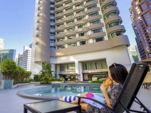 a woman sitting in a chair next to a swimming pool at Novotel Kuala Lumpur City Centre in Kuala Lumpur