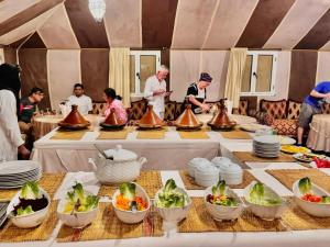 Un grupo de personas de pie alrededor de una mesa con comida. en Expedition Luxury camp, en Merzouga