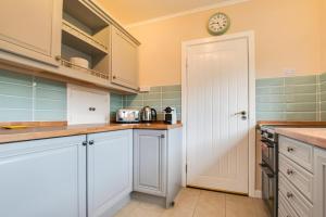 a kitchen with white cabinets and a clock on the wall at Murmur Y Llanw in Port-Eynon
