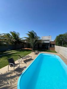 a blue swimming pool with two chairs and a house at Casa para temporada Diversão e sossego PRÓXIMA A PRAIA in Rio das Ostras