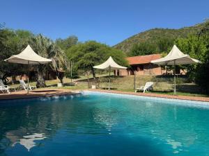 a swimming pool with white umbrellas and a house at Cabañas de la Colina in Villa General Belgrano