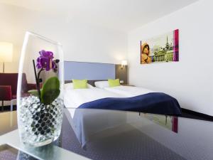 Radefeldにあるイビス スタイル ライプツィヒのベッド1台と紫の花の花瓶が備わるホテルルームです。 +114枚の写真