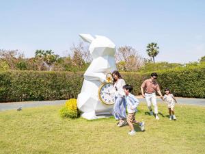 Una familia caminando frente a una escultura de reloj. en SO/ Sofitel Hua Hin, en Cha Am