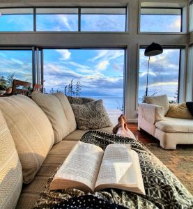 a woman laying on a couch with two open books at XSPOT Cliff House apartment, secluded 4WD location in Great Barrier Island