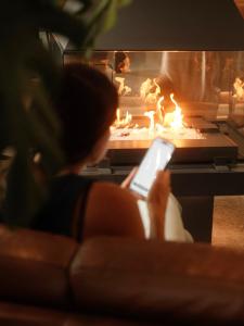 a woman sitting on a couch using a cell phone in front of a fireplace at Escapade bien-être, en Estrie in Shefford