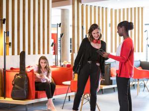 two women standing in a room with a woman looking at a cell phone at ibis Saint Quentin en Yvelines - Vélodrome in Montigny-le-Bretonneux