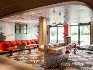 a waiting room with red chairs and a table at ibis Saint Quentin en Yvelines - Vélodrome in Montigny-le-Bretonneux