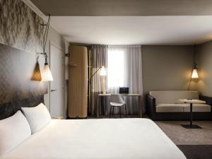a hotel room with a white bed and a couch at ibis Saint Quentin en Yvelines - Vélodrome in Montigny-le-Bretonneux