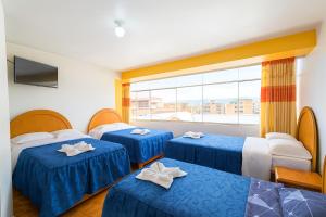 プーノにあるHOSTAL ACUARIUS PUNOのベッドが3つと窓があるホテルの部屋